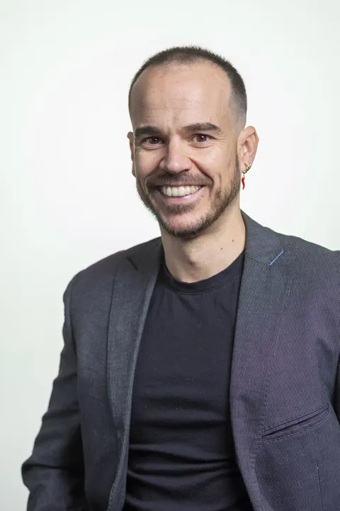 Retrato de Charlie sonriendo, con americana gris, sobre fondo blanco