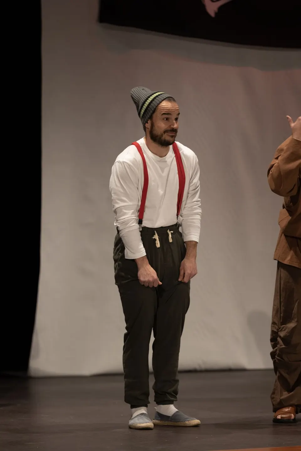 Charlie en escena con gorro de lana, camisa blanca y tirantes rojos