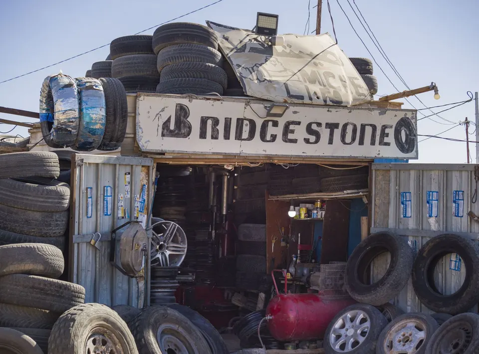 Taller de neumáticos en los campamentos, con ruedas apiladas bajo un cartel de Bridgestone