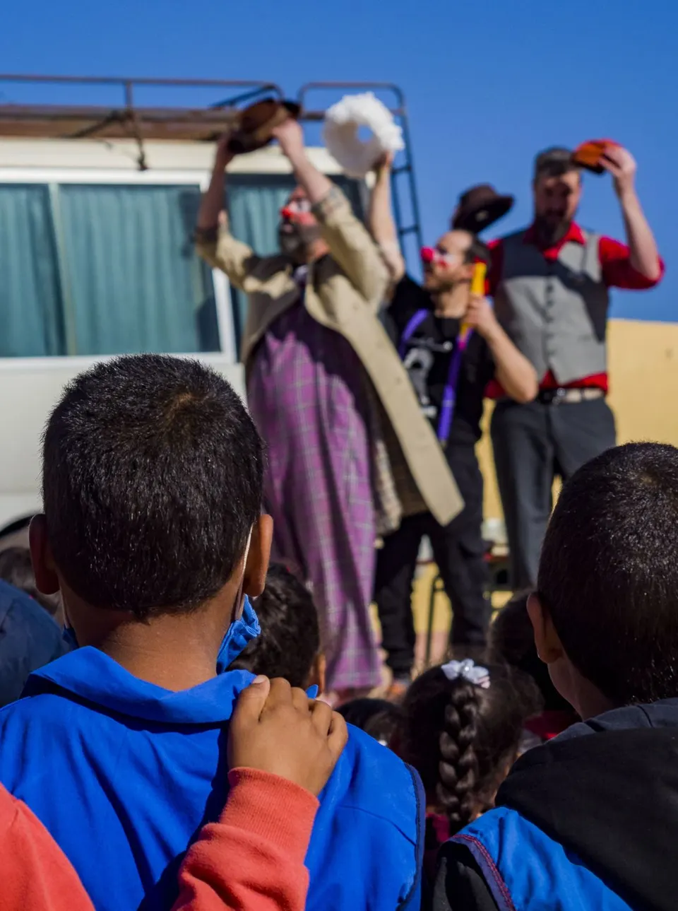Niños de espaldas miran a los magos, que actúan junto a un todoterreno