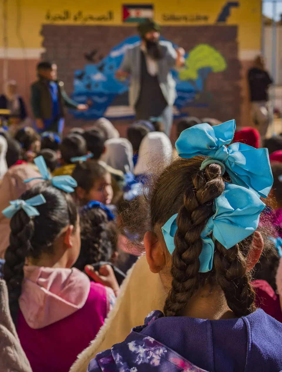 Niñas con lazos azules en el pelo miran el show ante un mural