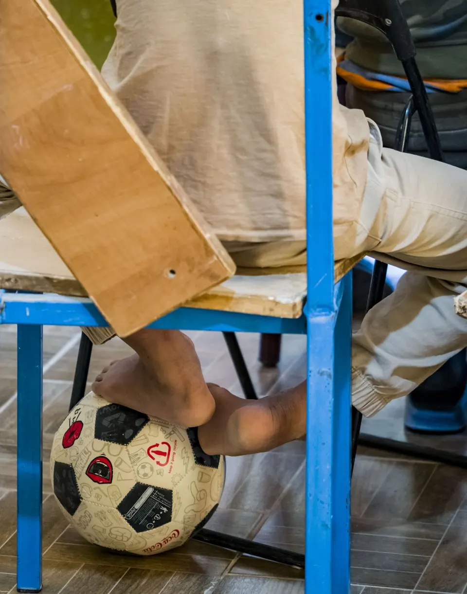 Un balón de fútbol bajo los pies de alguien sentado en una silla de colegio